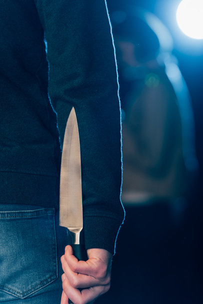 cropped view of murderer hiding knife behind back on black - Фото, зображення