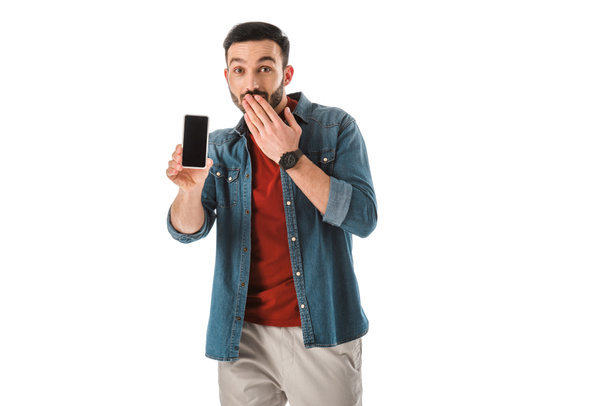 surprised bearded man covering mouth with hand while holding smartphone with blank screen isolated on white - Zdjęcie, obraz