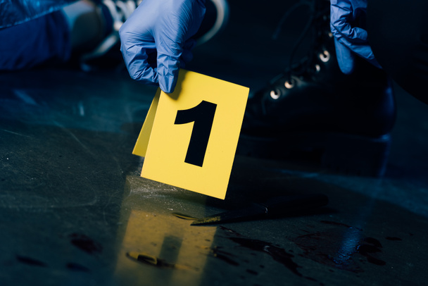 犯罪現場で証拠マーカーを持つゴム手袋の捜査官の部分的な見解 - 写真・画像