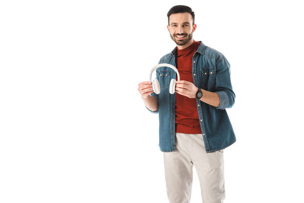 cheerful man looking at camera while holding headphones isolated on white - Valokuva, kuva