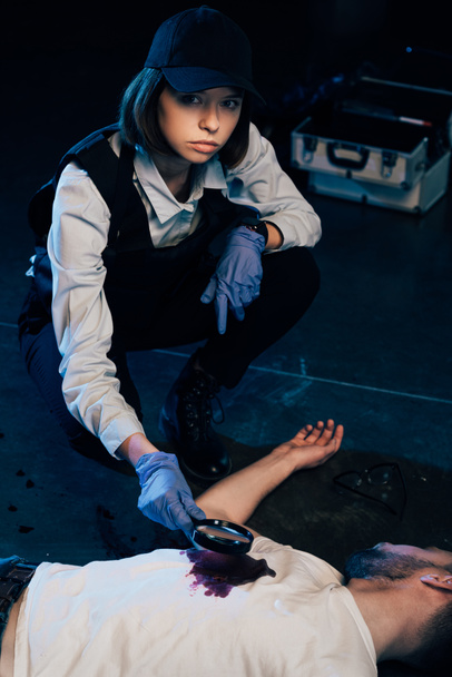 Investigador sentado cerca del cadáver y usando lupa en la escena del crimen
 - Foto, Imagen