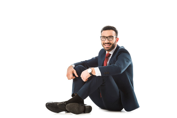 happy businessman in glasses looking at camera while sitting on white background - Foto, Bild