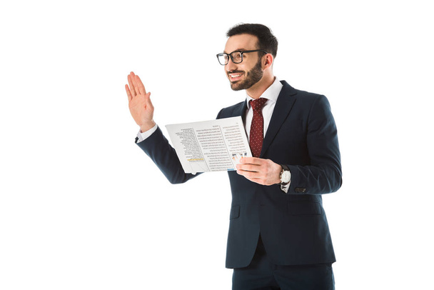 cheerful businessman with newspaper showing hello gesture and looking away isolated on white - Foto, afbeelding