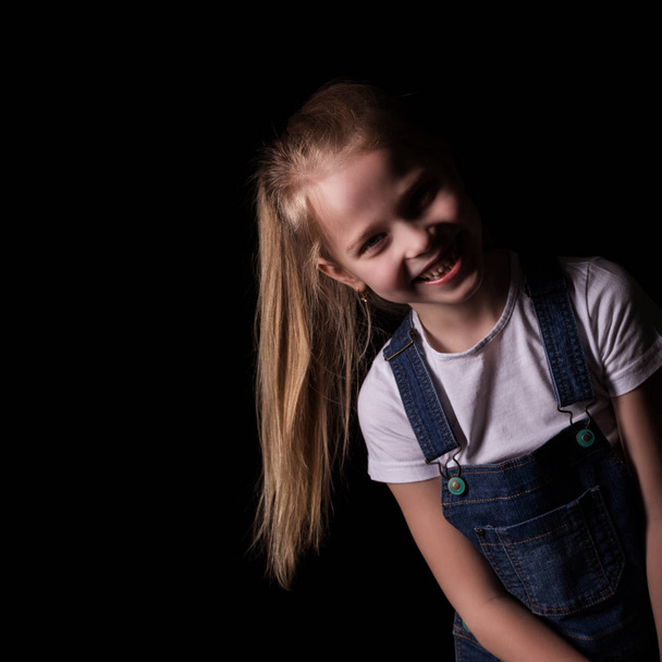 beautiful blonde little girl on a dark background. She stands in different poses and shows different emotions. free space for your text - Foto, Imagem
