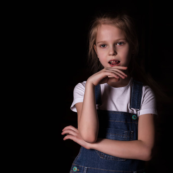 beautiful blonde little girl on a dark background. She stands in different poses and shows different emotions. free space for your text - 写真・画像