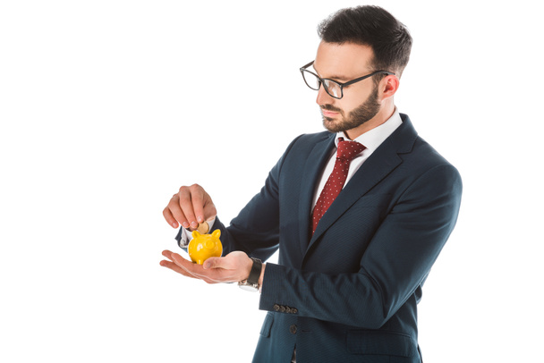 серьезный бородатый бизнесмен кладет монету в копилку, изолированную на белом
 - Фото, изображение