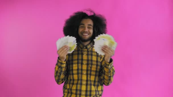 Young African American man holding cash money on purple background. - Filmagem, Vídeo