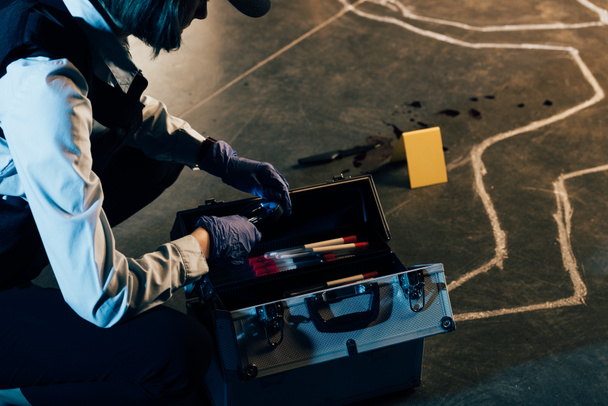 обрезанный вид следователя в резиновых перчатках с набором для расследования на месте преступления
 - Фото, изображение