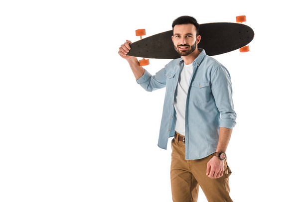 handsome smiling man holding longboard on shoulder and looking at camera isolated on white - Foto, immagini