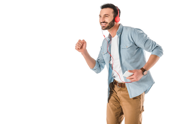 cheerful man dancing while listening music in headphones and holding smartphone isolated on white - Photo, image