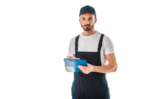serious delivery man writing on clipboard and looking at camera isolated on white - Photo, Image