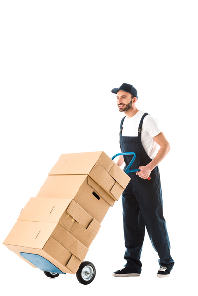 alegre guapo repartidor hombre transportando cajas de cartón cargadas en camión de mano aislado en blanco
 - Foto, Imagen