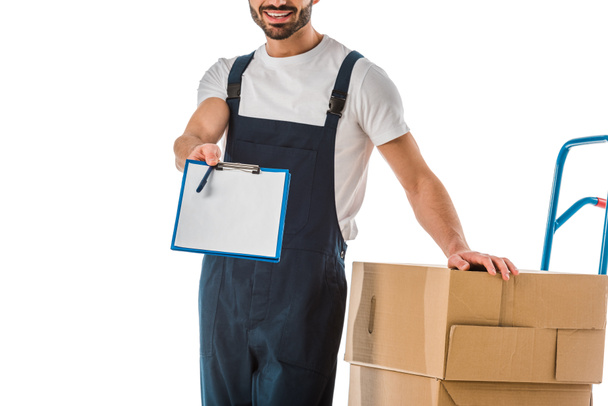 обрізаний вид доставки чоловік стоїть біля картонних коробок і тримає кишеню з чистим папером ізольовано на білому
 - Фото, зображення