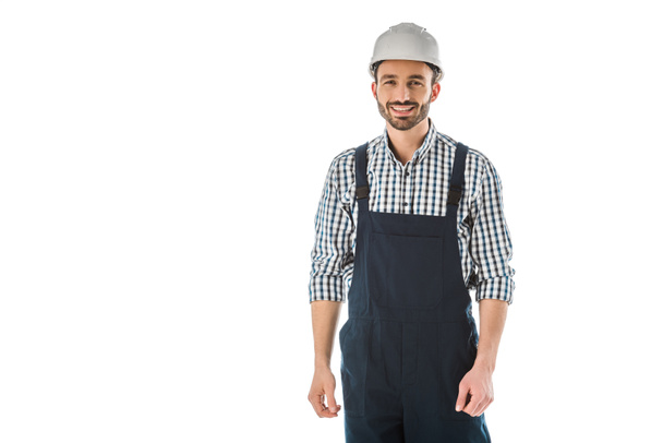 trabajador de la construcción sonriente en overoles y casco mirando a la cámara aislada en blanco
 - Foto, Imagen