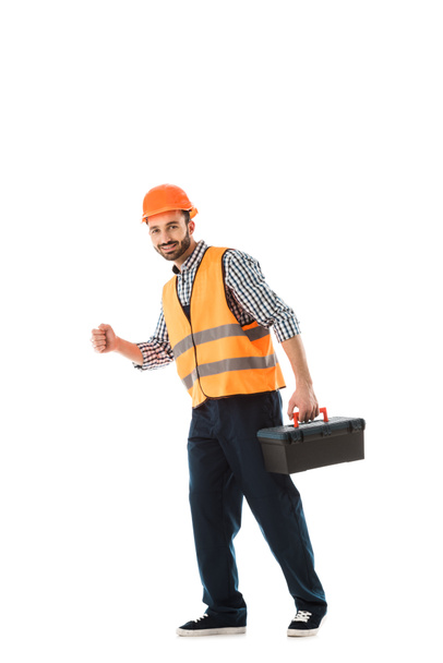 веселый строительный работник в спасательном жилете и шлеме холдинг ящик с инструментами изолированы на белом
 - Фото, изображение