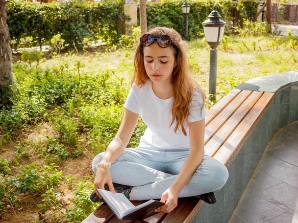Pretty yaoung girl reading a book on a bench in a park - Foto, Imagem