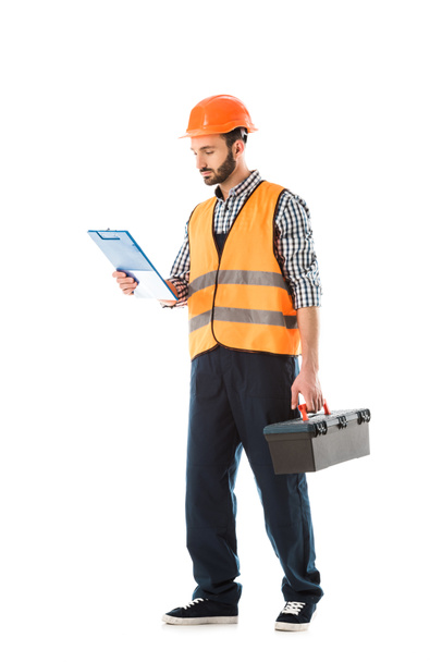 serious construction worker holding toolbox and looking at clipboard isolated on white - Fotoğraf, Görsel