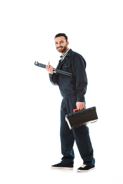 cheerful plumber with toolbox and adjustable wrench showing middle finger while smiling at camera isolated on white - Photo, Image