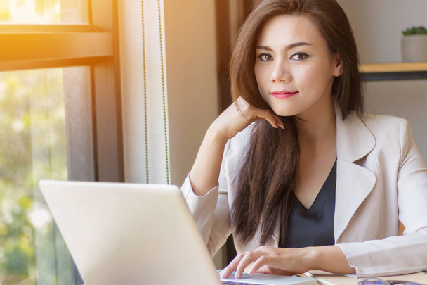 startup business in Asia concept. focused young Asian business woman with thinking face working with laptop at workplace looking at camera, film effect and sun flare effect. - Photo, image