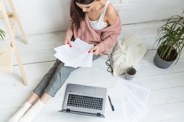 Young woman sits on the floor in a Scandinavian apartment interior with a laptop, studying law, freelance girl at work, distance learning student, online employment, paperwork and outsourcing concept - 写真・画像