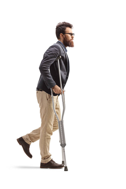Full length profile shot of a young bearded man walking with crutches isolated on white background - Φωτογραφία, εικόνα