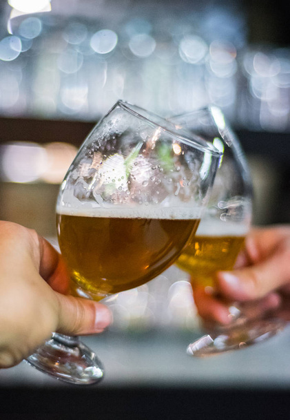 Close-up view of a two glass of beer in hand. Beer glasses clinking in bar or pub - Foto, Imagem