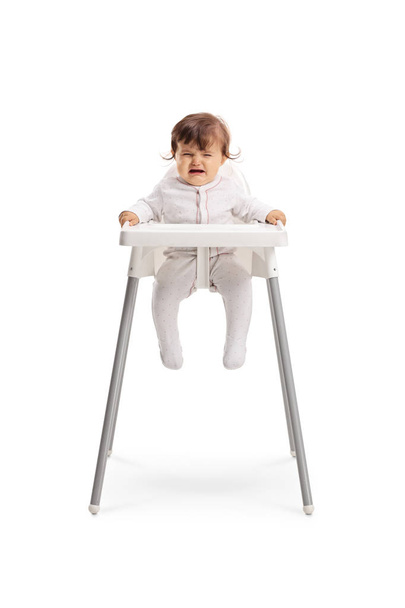 Full length portrait of a baby girl sitting in a baby chair and crying isolated on white background - Photo, Image