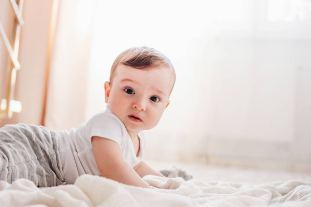 Sevimli küçük bebek erkek 6 ay evde beyaz battaniye üzerinde kamera bakıyor - Fotoğraf, Görsel