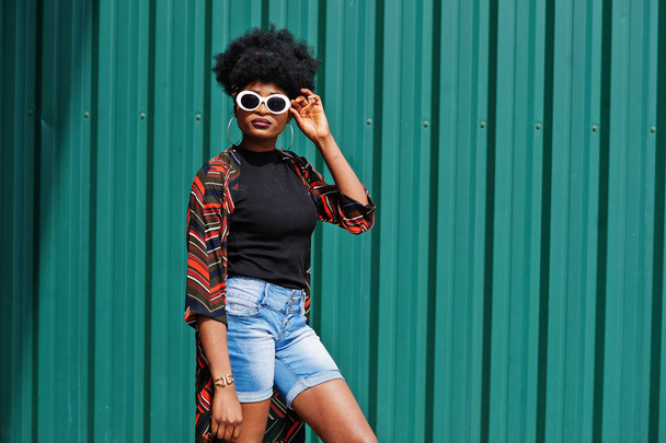 African woman with afro hair, in jeans shorts and white sunglass - Foto, Imagen