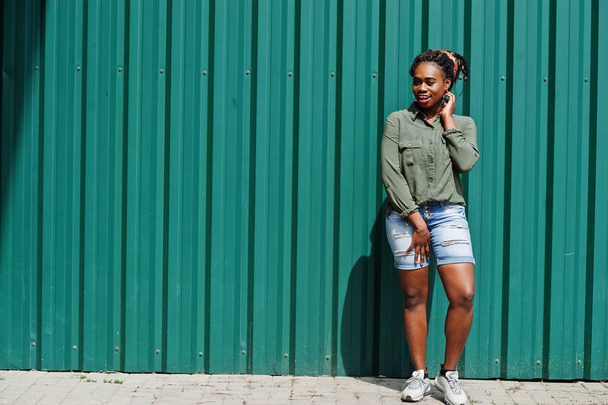 African woman with dreads hair, in jeans shorts posed against gr - Photo, Image