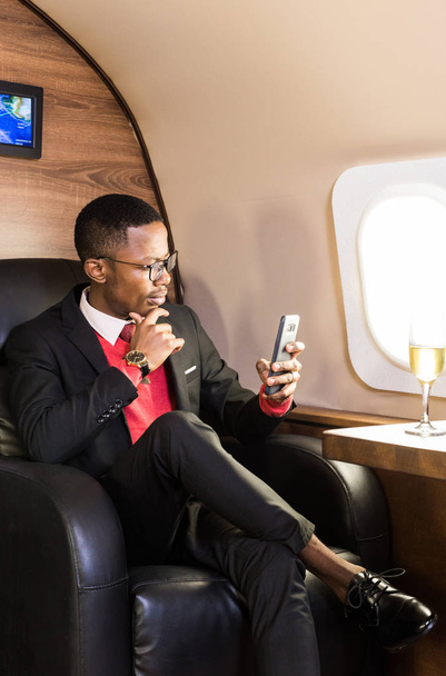 Successful young Afro American black businessman sitting in the chair of his private jet - Foto, immagini