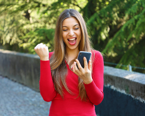Mujer eufórica mirando su teléfono inteligente al aire libre
 - Foto, Imagen