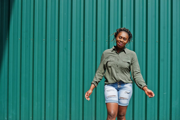 African woman with dreads hair, in jeans shorts posed against gr - Foto, Imagem