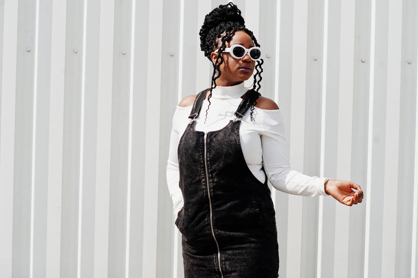 African woman in denim overalls skirt, white sunglasses posed ag - Foto, afbeelding