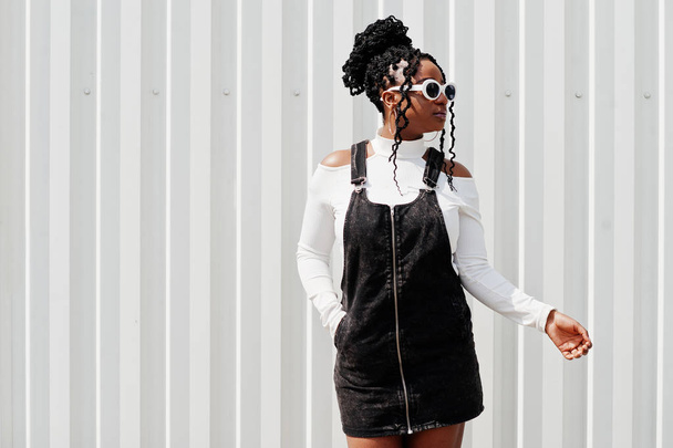 African woman in denim overalls skirt, white sunglasses posed ag - Foto, Bild
