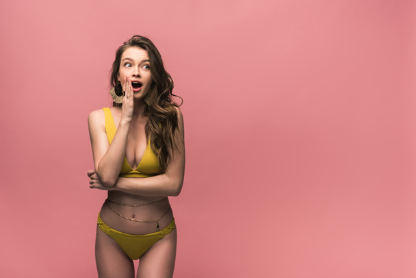 impactado joven mujer en traje de baño amarillo mirando hacia otro lado aislado en rosa
 - Foto, imagen