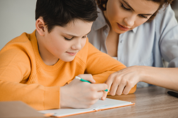 beautiful woman helping attentive son doing schoolwork at home - Photo, Image