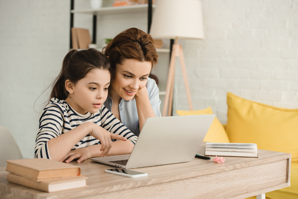здивована мати і дочка використовують ноутбук під час виконання домашнього завдання разом
 - Фото, зображення