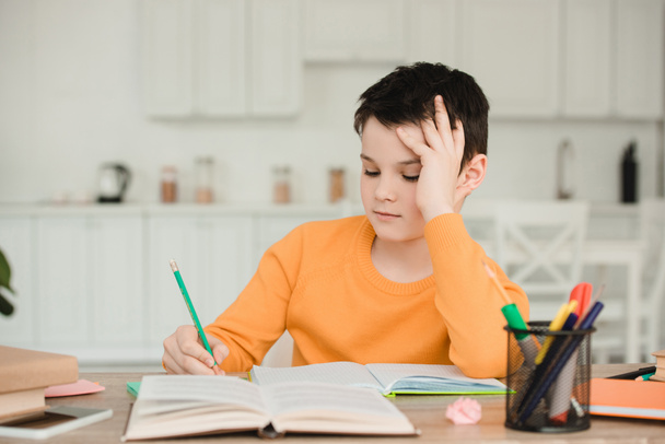 προσεκτικός μαθητής διαβάζοντας το βιβλίο και γράφοντας ενώ κάνει σχολικές εργασίες στο σπίτι - Φωτογραφία, εικόνα