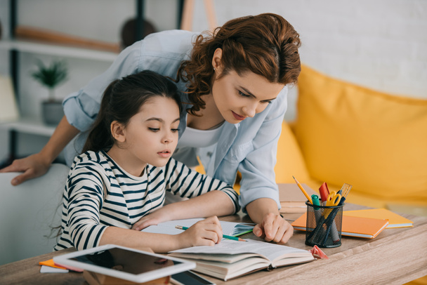 attentive mother helping adorable daughter doing schoolwork at home - Foto, Imagem