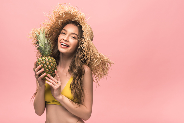smiling girl in straw hat holding pineapple isolated on pink - Foto, Imagen