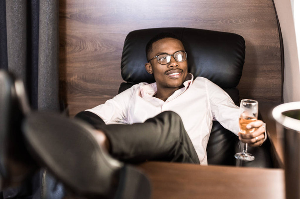 Successful young Afro American black businessman sitting in the chair of his private jet - 写真・画像