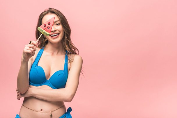 attractive young woman in swimsuit holding watermelon lollipop isolated on pink - Foto, immagini
