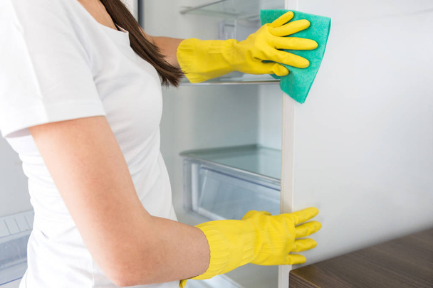 Nuori nainen siivousfirmasta siivoaa kotona. Mies pesee keittiön pesee jääkaapin keltaisilla hanskoilla siivoustarvikkeilla. - Valokuva, kuva