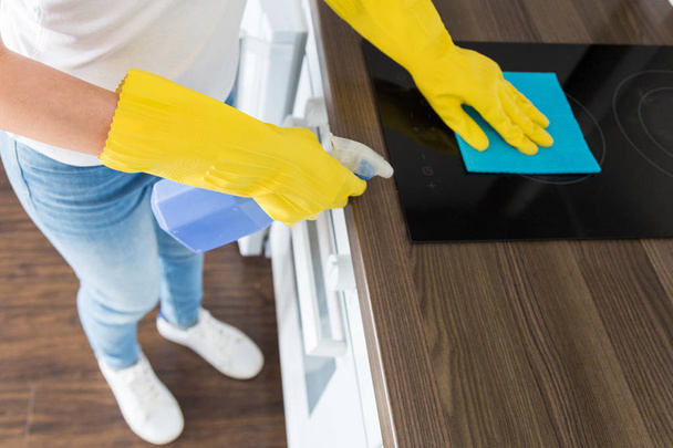 Profesyonel temizlik şirketinden genç bir kadın evi temizliyor. Bir adam mutfağı temizlik malzemeleriyle sarı eldivenlerle yıkıyor.. - Fotoğraf, Görsel
