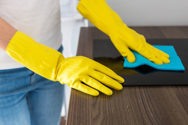 Молода жінка з професійної клінінгової компанії прибирає вдома. Чоловік миє кухню в жовтих рукавичках з речами для прибирання
. - Фото, зображення