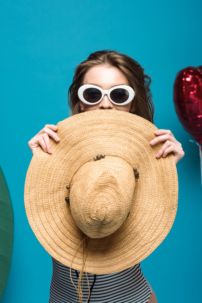 happy young woman in sunglasses holding straw hat on blue - Fotoğraf, Görsel