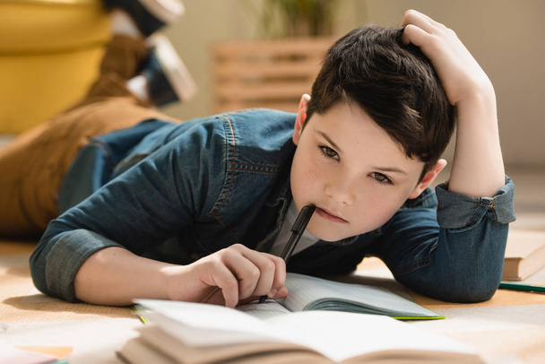 селективное внимание вдумчивого мальчика, лежащего на полу рядом с копировальной книгой, делая домашнюю работу
 - Фото, изображение