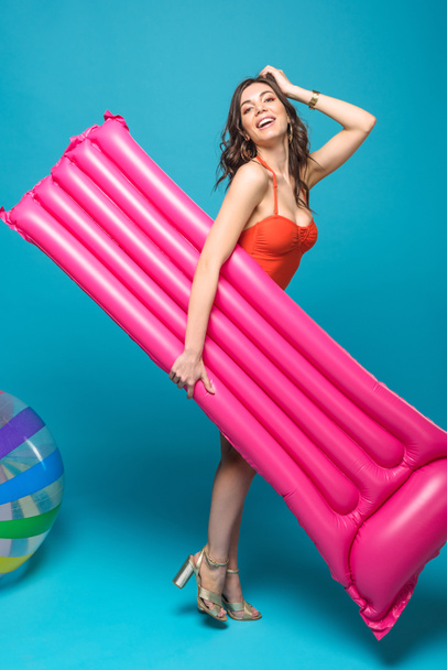 full length view of smiling woman in swimsuit holding inflatable swimming mattress on blue - Fotografie, Obrázek