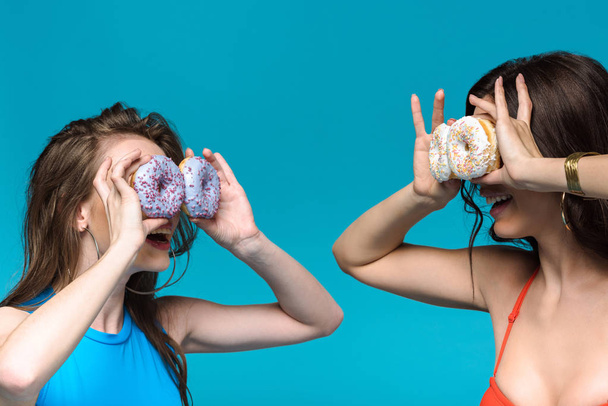 two girls in swimsuits holding donuts isolated on blue - Foto, afbeelding